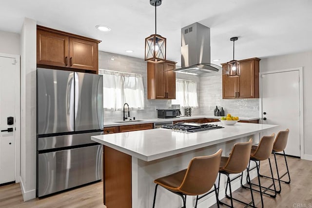 kitchen with stainless steel appliances, a kitchen island, ventilation hood, light hardwood / wood-style flooring, and hanging light fixtures