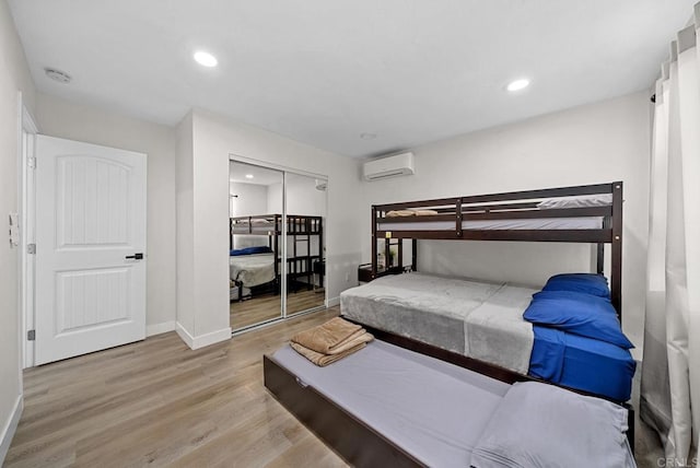 bedroom with a closet, a wall mounted AC, and light wood-type flooring