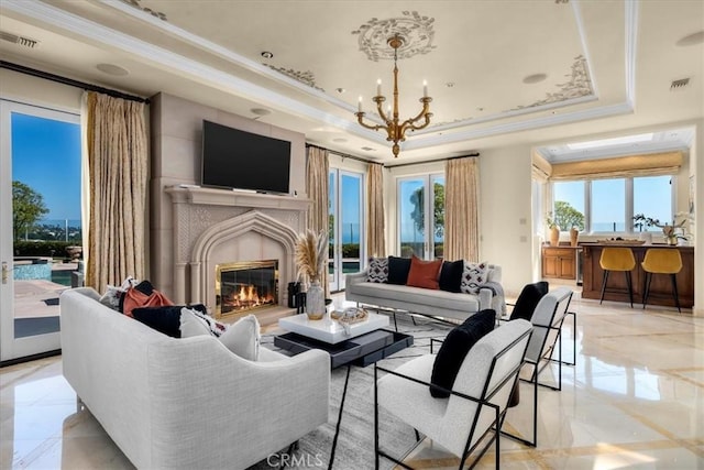 living room featuring plenty of natural light, a fireplace, a chandelier, and a tray ceiling