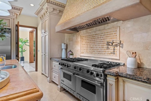 kitchen with cream cabinetry, custom range hood, backsplash, and stainless steel appliances