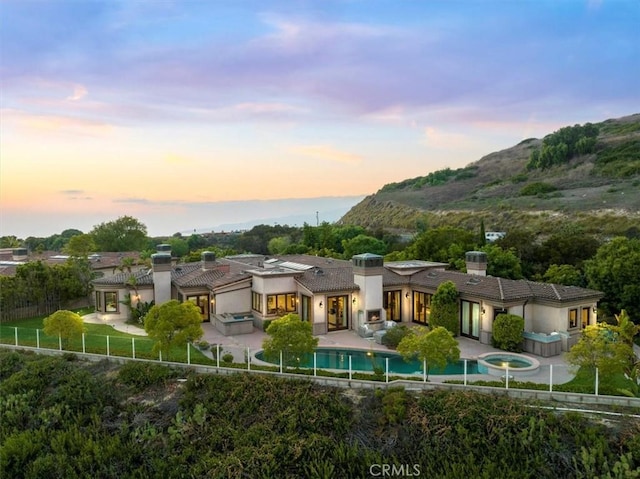 back house at dusk featuring a mountain view, a swimming pool with hot tub, and a patio area