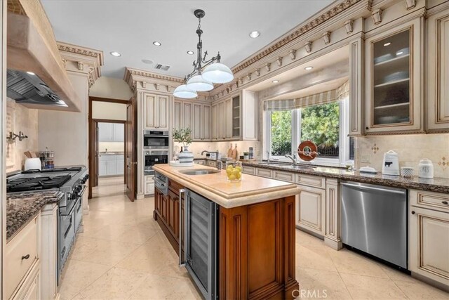 kitchen with cream cabinetry, wall chimney exhaust hood, beverage cooler, and appliances with stainless steel finishes