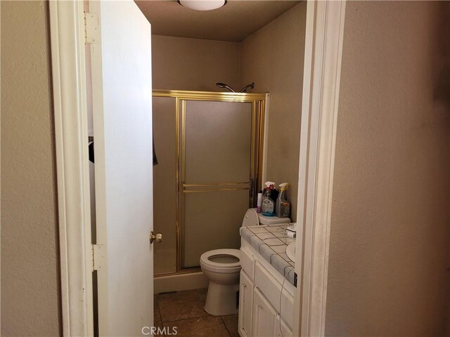 bathroom with tile patterned flooring, vanity, toilet, and a shower with door