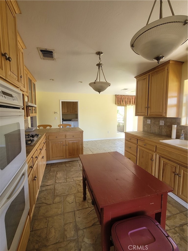 kitchen with decorative light fixtures, white double oven, dark tile flooring, backsplash, and sink