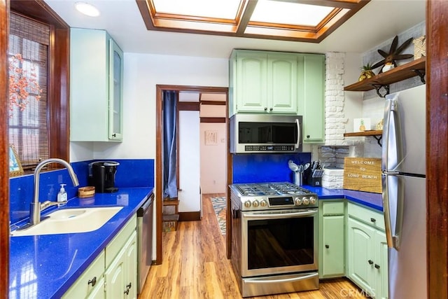 kitchen featuring light hardwood / wood-style floors, sink, green cabinets, a skylight, and appliances with stainless steel finishes