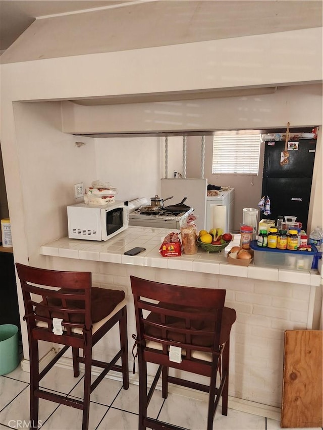 kitchen featuring tile counters, light tile patterned floors, separate washer and dryer, and range