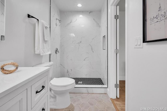 bathroom featuring vanity, a tile shower, tile flooring, and toilet