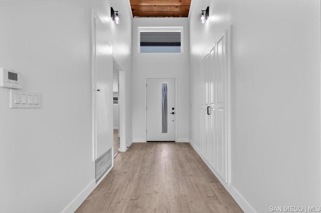 corridor featuring a towering ceiling, light hardwood / wood-style flooring, and wood ceiling