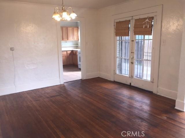 empty room with a chandelier, french doors, dark hardwood / wood-style flooring, and crown molding