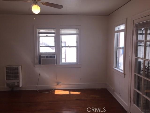 unfurnished room featuring cooling unit, a healthy amount of sunlight, dark wood-type flooring, and heating unit