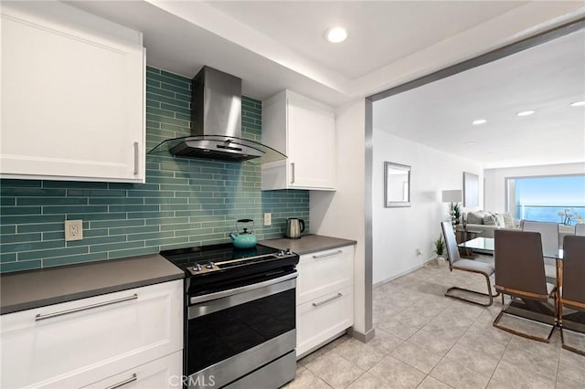 kitchen with stainless steel electric range, backsplash, wall chimney range hood, and white cabinetry