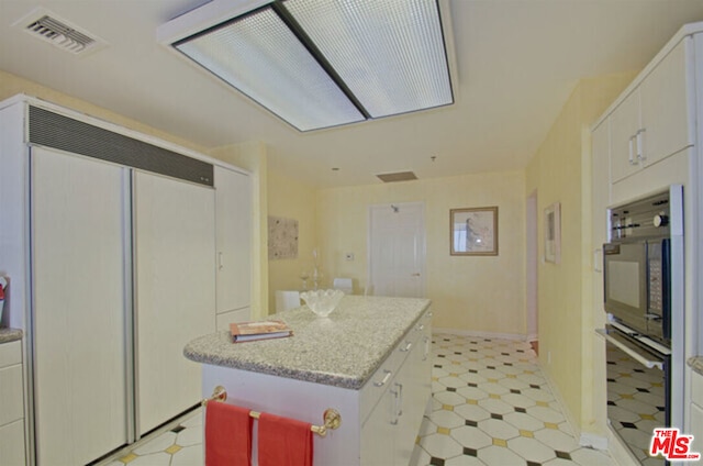 kitchen featuring paneled fridge, a center island, and white cabinetry