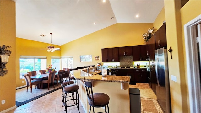 kitchen featuring light tile flooring, ceiling fan, a kitchen bar, dark brown cabinetry, and light stone countertops