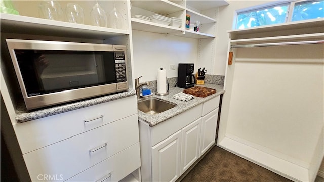 kitchen featuring light stone counters, white cabinetry, dark colored carpet, and sink