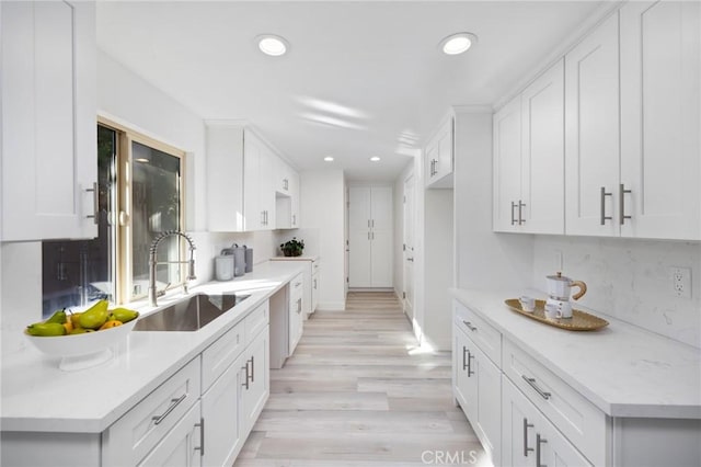 kitchen featuring white cabinets, backsplash, light hardwood / wood-style floors, and sink