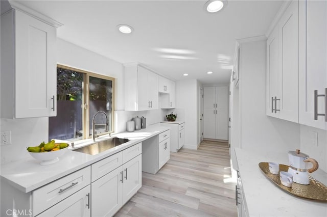 kitchen with white cabinetry, sink, light stone counters, and light hardwood / wood-style flooring