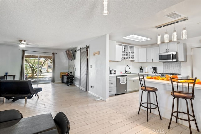 kitchen featuring appliances with stainless steel finishes, a barn door, decorative light fixtures, light hardwood / wood-style flooring, and a breakfast bar area