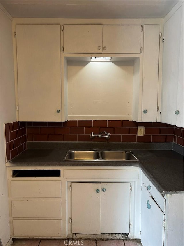 kitchen with tasteful backsplash, dark countertops, white cabinets, and a sink