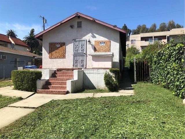 bungalow with stucco siding, fence, and a front yard