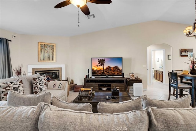 tiled living room featuring ceiling fan with notable chandelier and vaulted ceiling