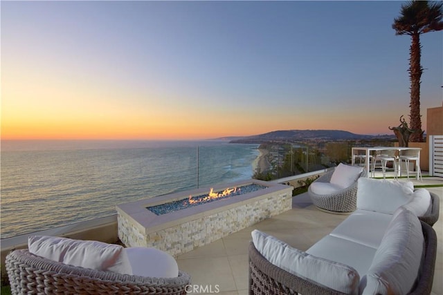 patio terrace at dusk featuring a water view and an outdoor living space with a fire pit