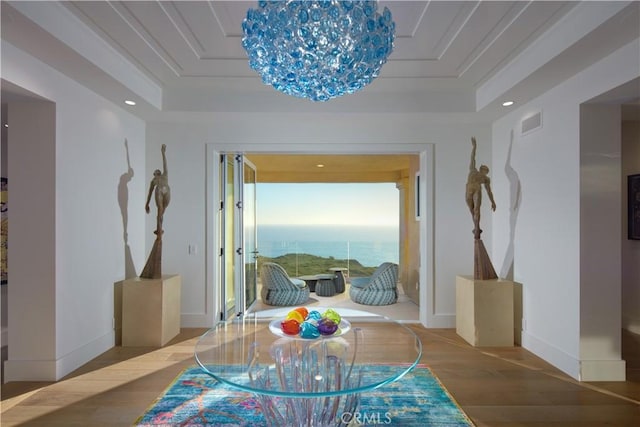 interior space featuring a raised ceiling, a water view, wood-type flooring, and a notable chandelier