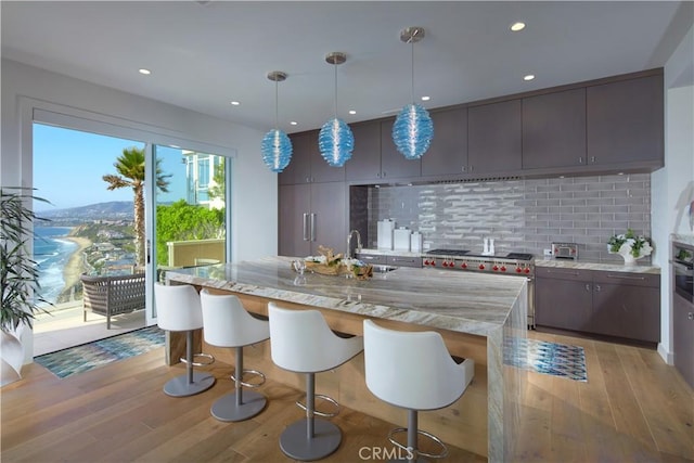 kitchen featuring light wood-type flooring, decorative light fixtures, high end stainless steel range oven, and backsplash