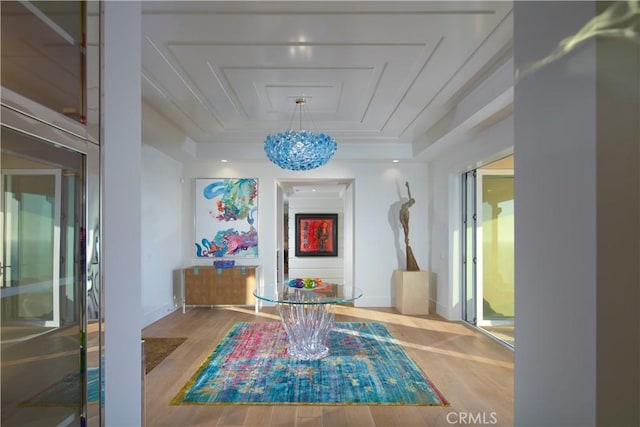 hallway featuring a tray ceiling, wood-type flooring, and a notable chandelier