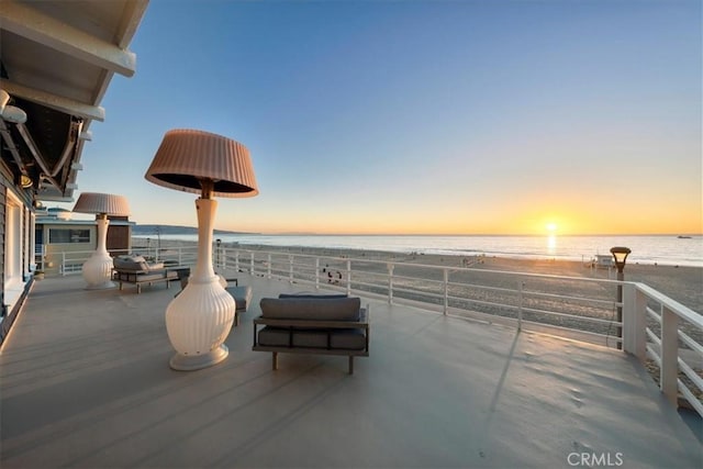 patio terrace at dusk with a water view, a beach view, and a balcony