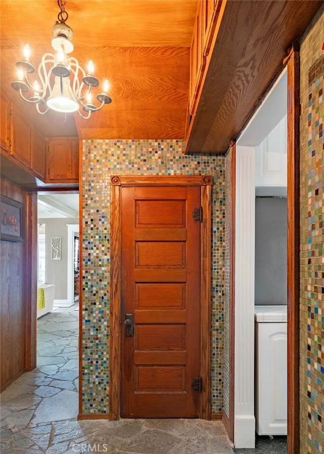 hallway with an inviting chandelier, brick wall, and lofted ceiling