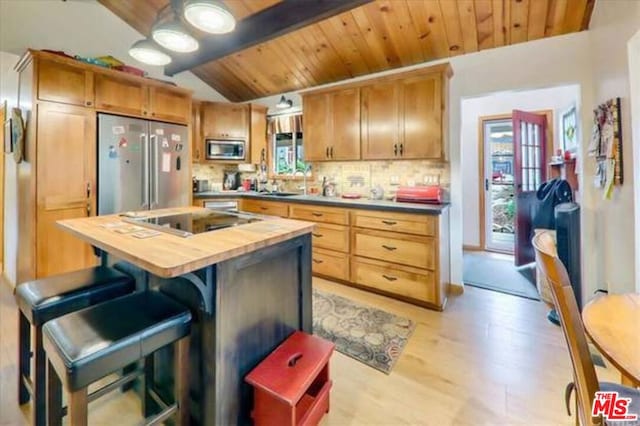 kitchen with wood counters, appliances with stainless steel finishes, wooden ceiling, vaulted ceiling with beams, and a kitchen island