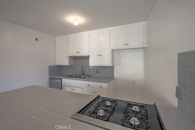 kitchen featuring decorative backsplash, stainless steel dishwasher, sink, white cabinetry, and tile counters