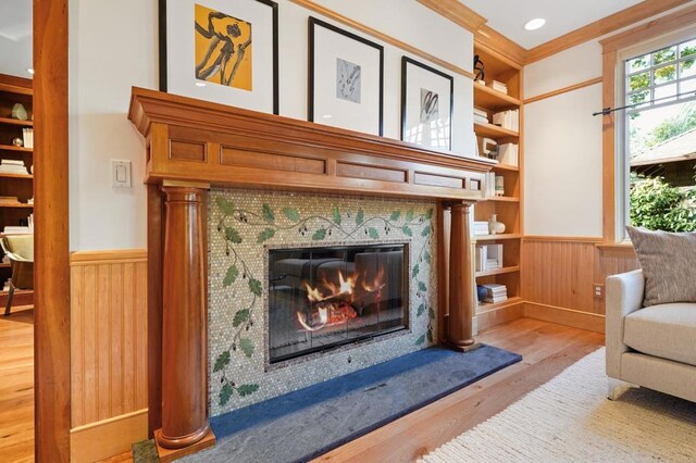 living area featuring wooden walls, built in features, wood-type flooring, ornamental molding, and a tile fireplace