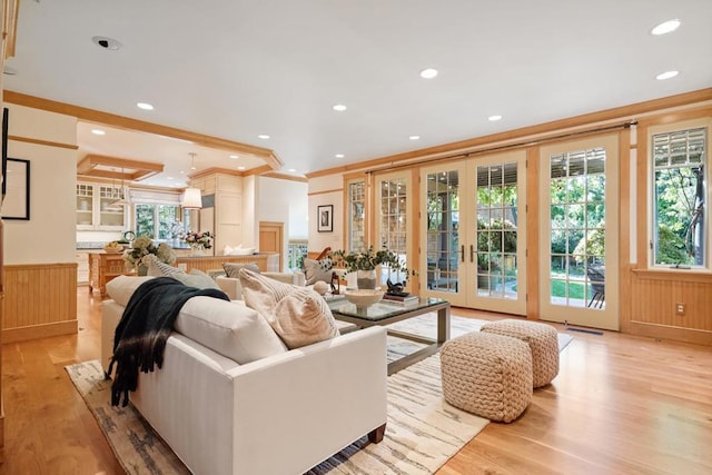 living room with french doors, wood walls, crown molding, and light hardwood / wood-style flooring