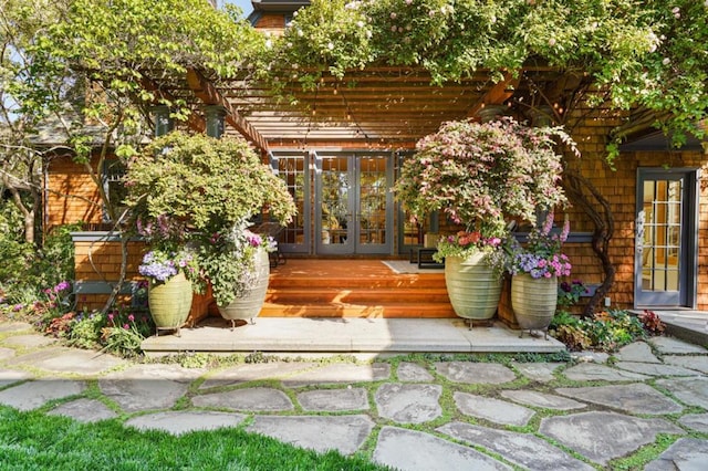 view of exterior entry featuring a pergola, a wooden deck, and french doors