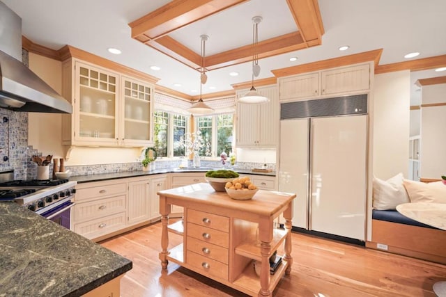 kitchen featuring stainless steel range with gas cooktop, a tray ceiling, hanging light fixtures, paneled refrigerator, and wall chimney exhaust hood