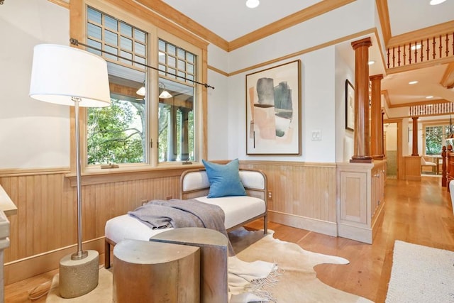 living area featuring light hardwood / wood-style floors, crown molding, wood walls, and ornate columns