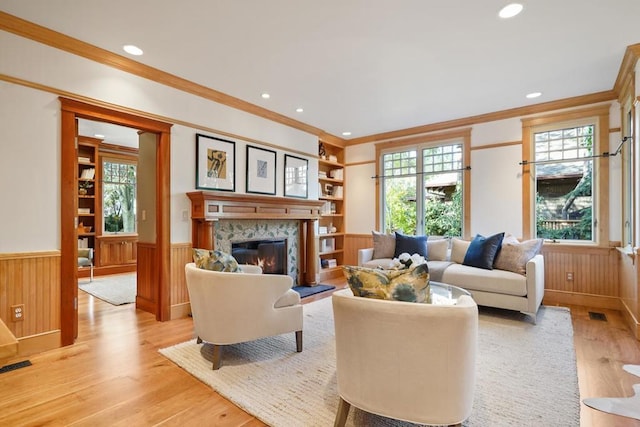 living room featuring light wood-type flooring, built in features, ornamental molding, and a fireplace