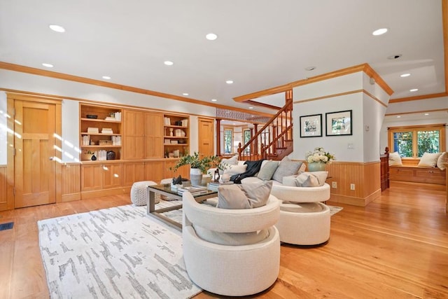 living room with ornamental molding, light hardwood / wood-style floors, and wood walls