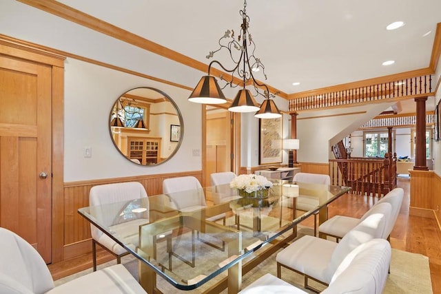 dining room featuring light hardwood / wood-style floors, crown molding, ornate columns, and wooden walls