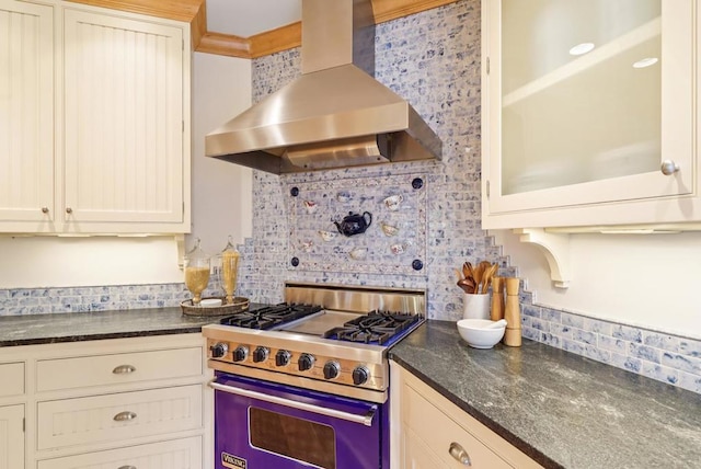 kitchen featuring stainless steel range, wall chimney exhaust hood, decorative backsplash, and dark stone countertops