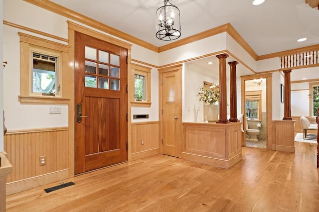 entrance foyer featuring ornate columns, an inviting chandelier, wood walls, ornamental molding, and light hardwood / wood-style flooring