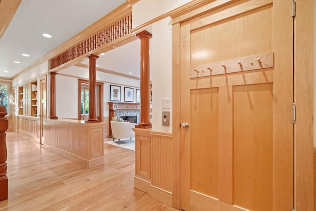 corridor featuring light wood-type flooring, crown molding, and ornate columns