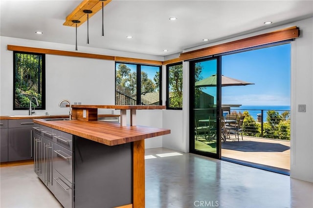 kitchen featuring sink, a water view, an island with sink, and wood counters