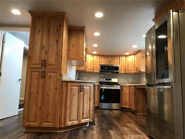 kitchen featuring light stone countertops, backsplash, stainless steel appliances, dark wood-type flooring, and sink