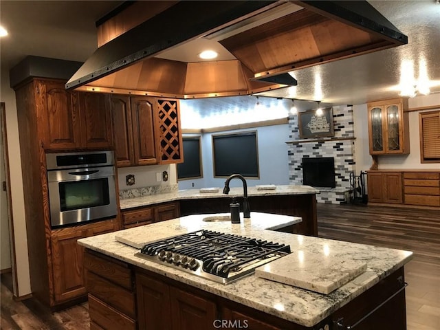 kitchen featuring appliances with stainless steel finishes, light stone counters, sink, dark hardwood / wood-style floors, and an island with sink