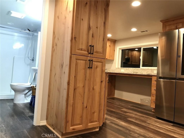 kitchen featuring light stone countertops, built in desk, dark hardwood / wood-style floors, and stainless steel refrigerator