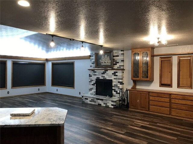 living room with a textured ceiling, a fireplace, dark wood-type flooring, and track lighting