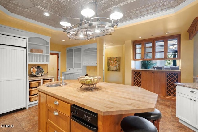 kitchen with wood counters, a center island with sink, ornamental molding, white cabinets, and sink