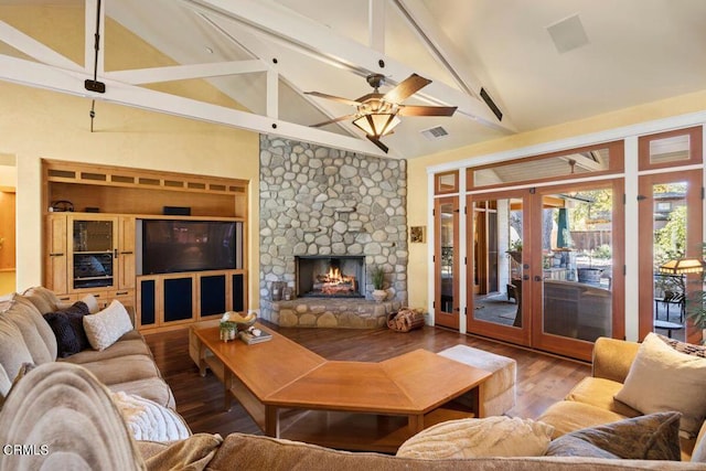 living room with hardwood / wood-style flooring, a stone fireplace, ceiling fan, french doors, and beam ceiling